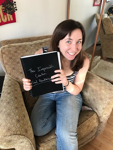 Author Betsy Flak holding a black bound notebook entitled 'The Impossible Creation: Final Readthrough.'